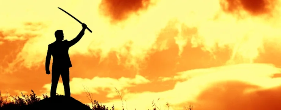 Silhouette of person in a suit holding. sword against an amber sunset. 