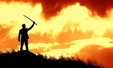 Silhouette of person in a suit holding. sword against an amber sunset. 
