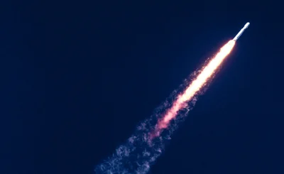 Rocket on a deep blue sky flies towards top right, leaving a long trail of flame