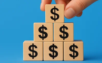 Building blocks with dollar signs. Hand placing a block on the top of the pyramid