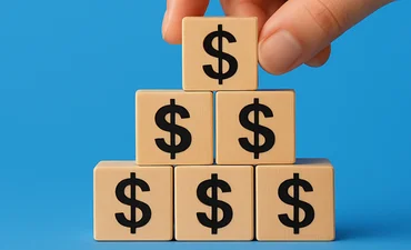 Building blocks with dollar signs. Hand placing a block on the top of the pyramid