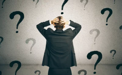 Business person staring at concrete wall covered in question marks, uncertainty concept © peshkov - Canva.com