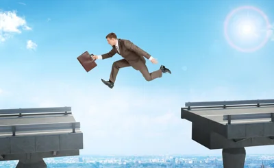 Man in suit with suitcase jumps over gap in road. 